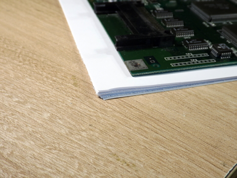 Amiga mainboard lying on stacked sheets of paper.